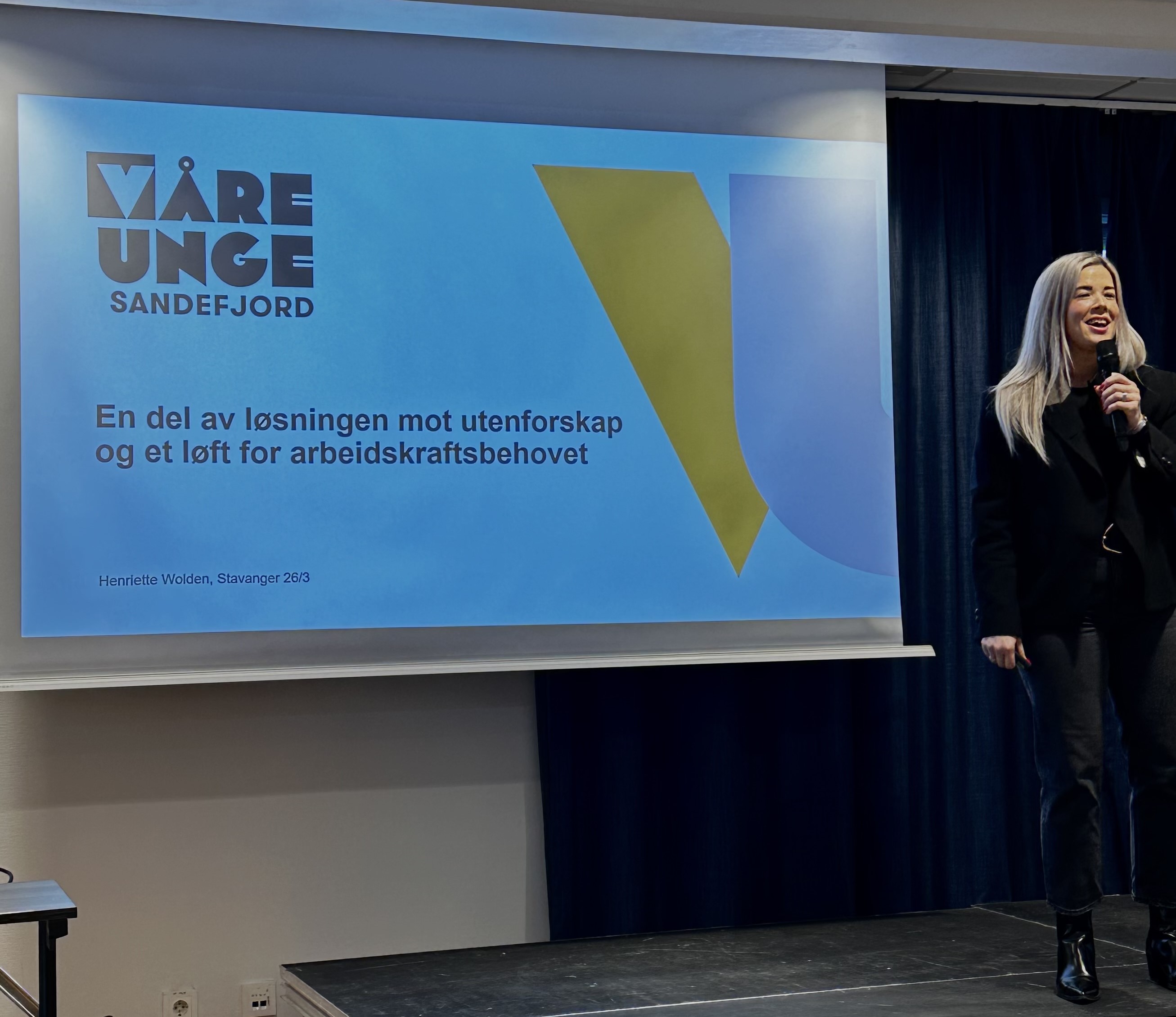 Wolden på scenen foran en skjerm med presentasjon.