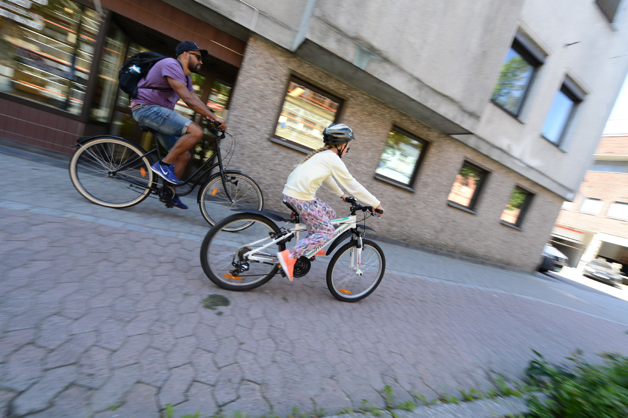 Foto av to syklister, en voksen, ett barn, i fart på belegningsstein