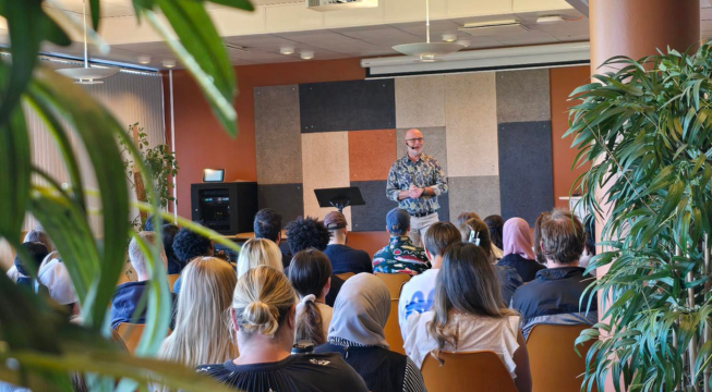 Rektor står foran elevene i kantina og holder åpningstale.