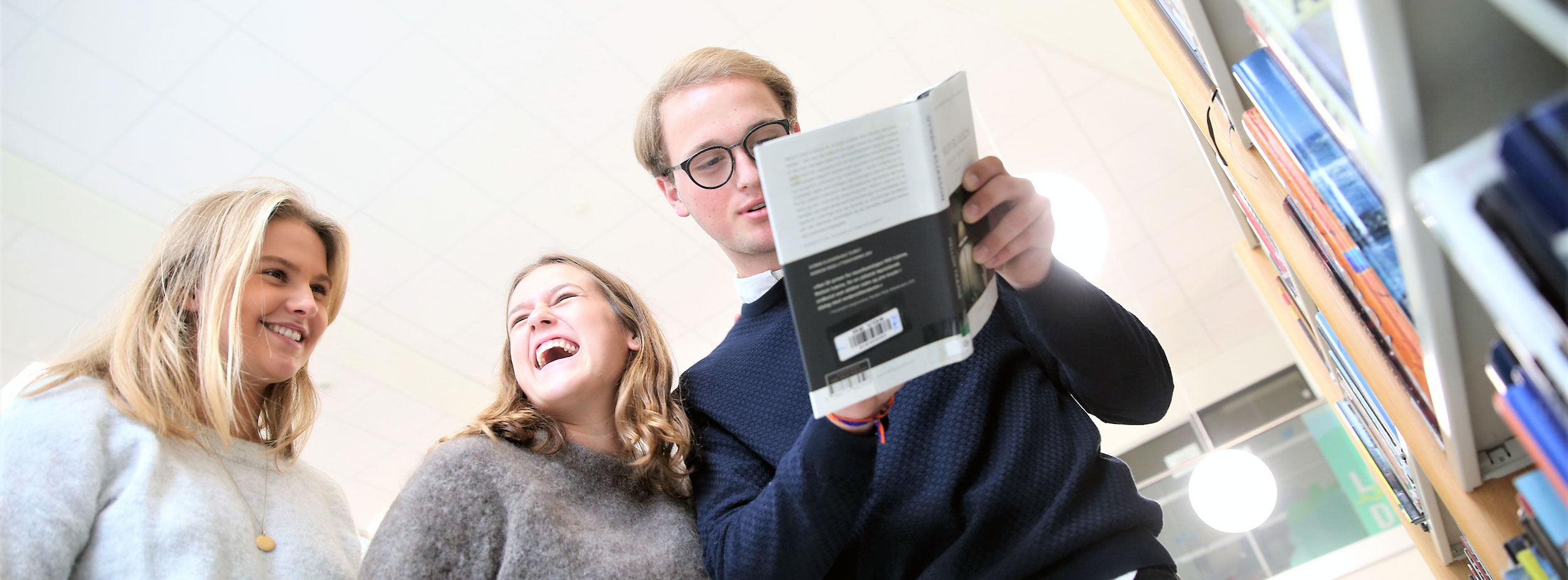 To jenter og en gutt som smiler og leser en bok