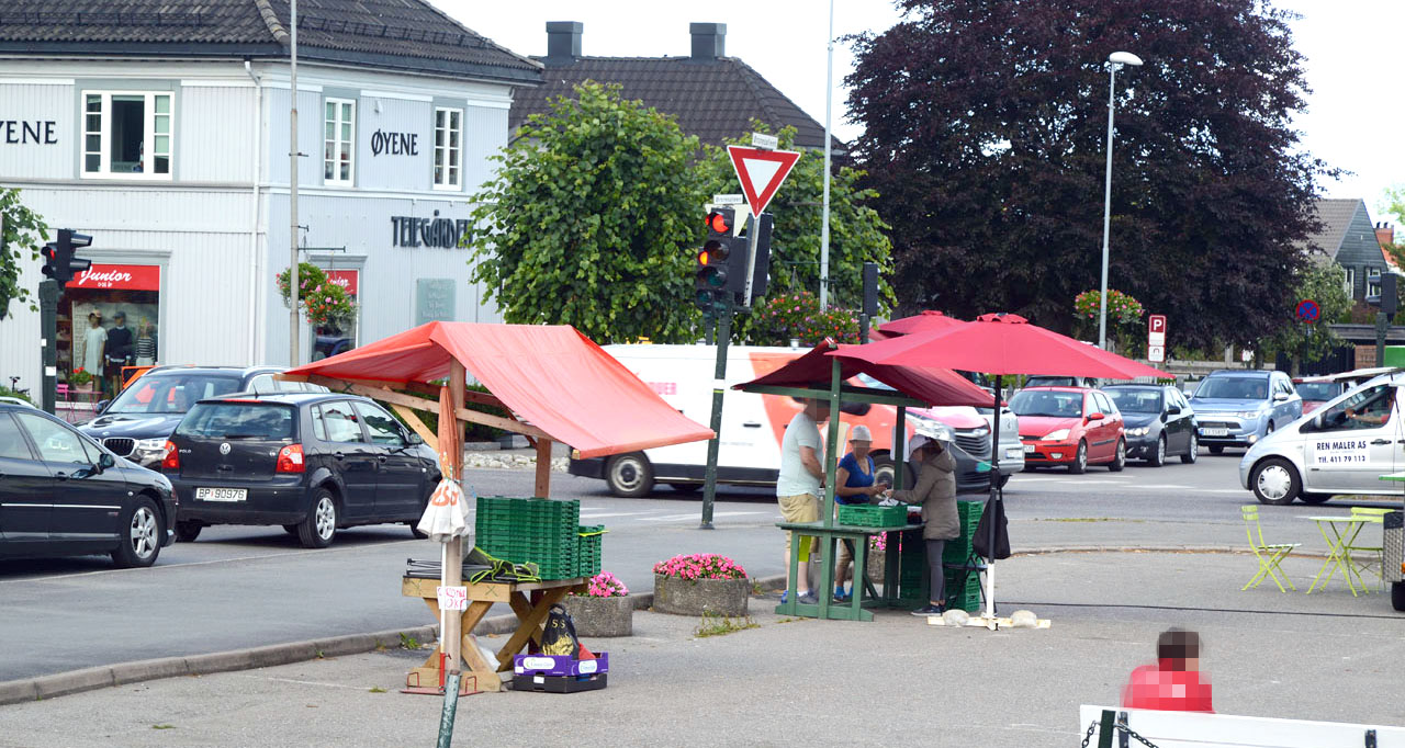 Foto av Teie torv med torgboder, mennesker som handler og trafikk i bakgrunnen