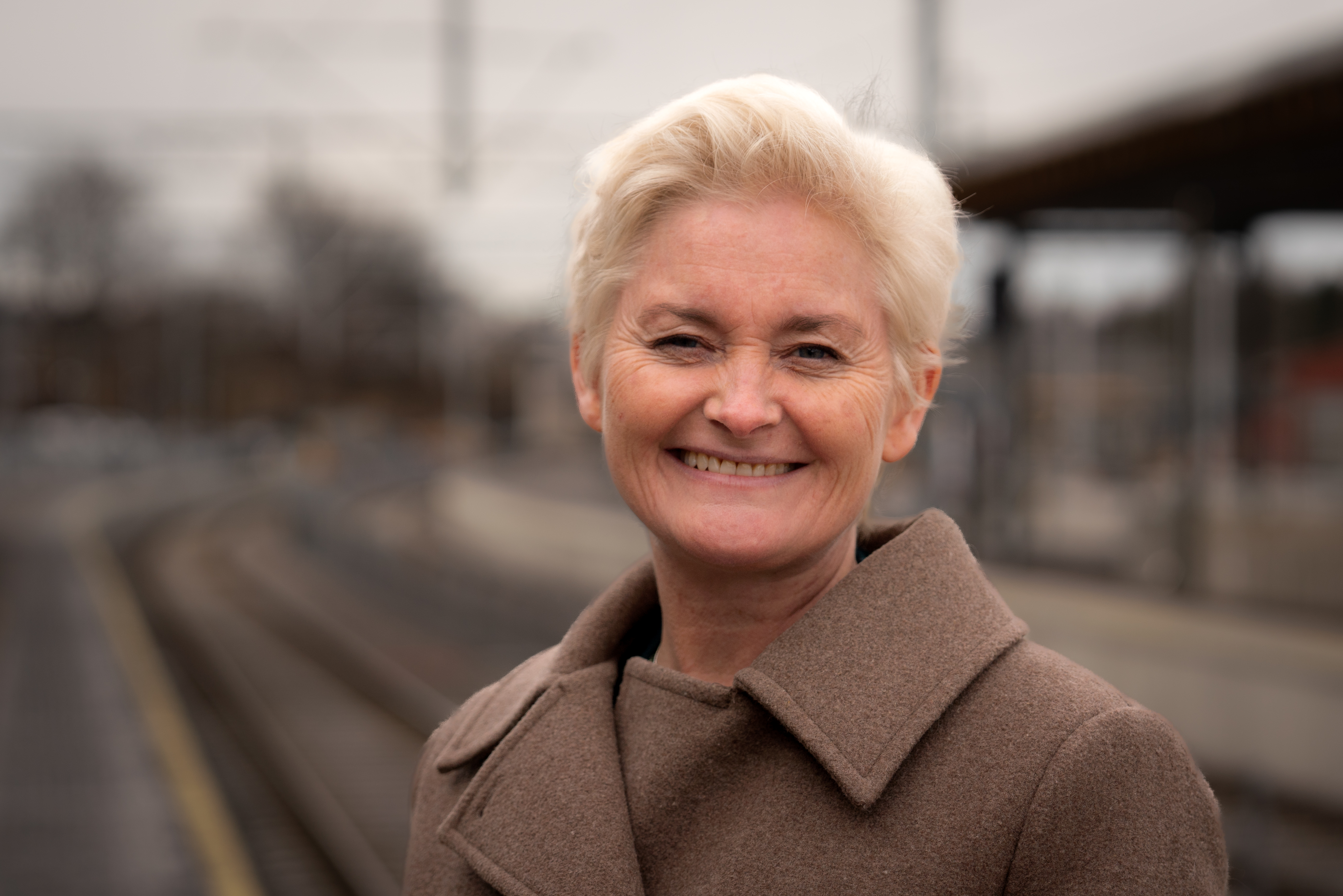 Foto av fylkesordfører i Vestfold, Anne Strømøy med jernbanestasjon og togskinner i bakgrunnen