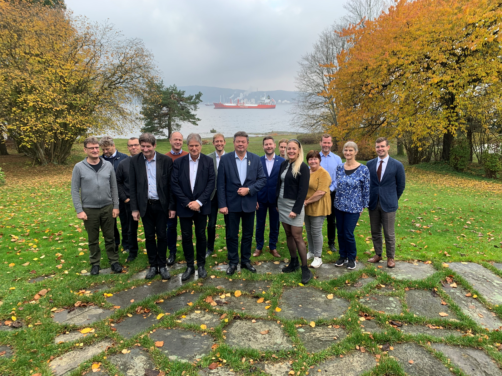 Gruppebilde av Nordsjøkommisjonens transportgruppe, der hagen rundt Adminiet på Herøya og Frierfjorden er synlig i bakgrunnen.