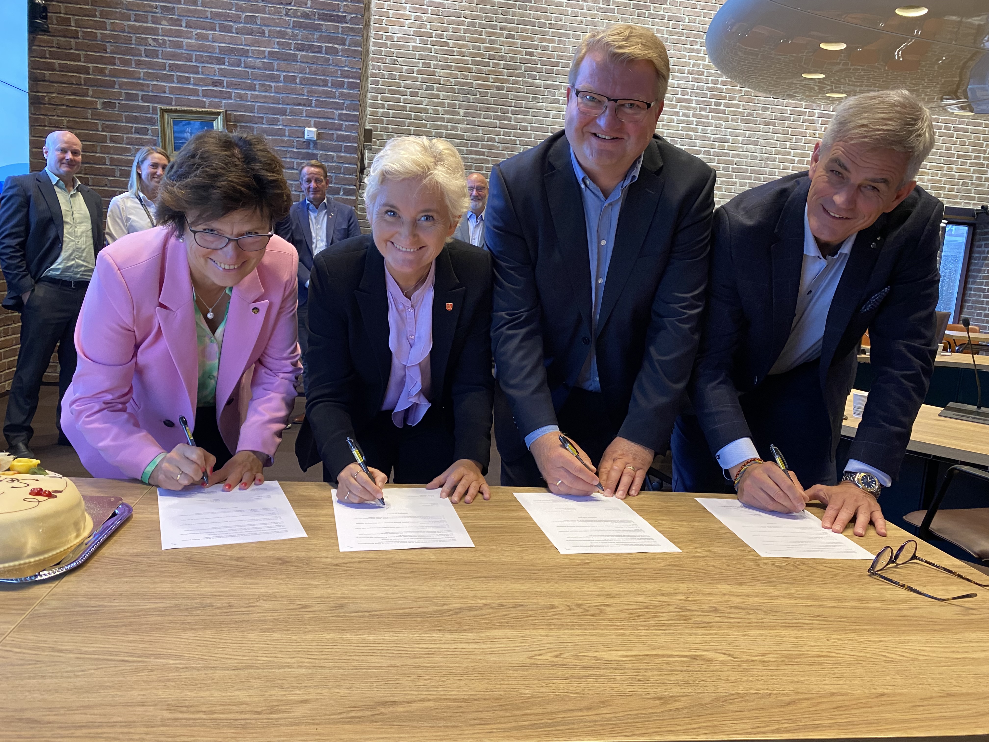 De fire som signerte avtalen ser i kamera og holder i hver sin penn som de skal til og signere avtalen med.