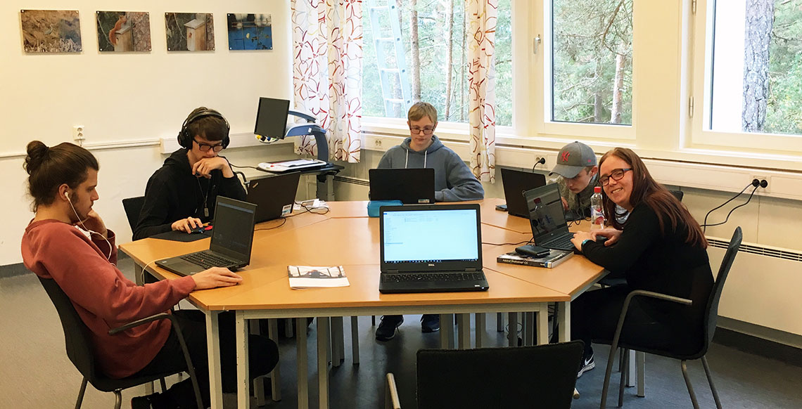 5 ungdommer sitter rundt et bord med hver sin laptop.