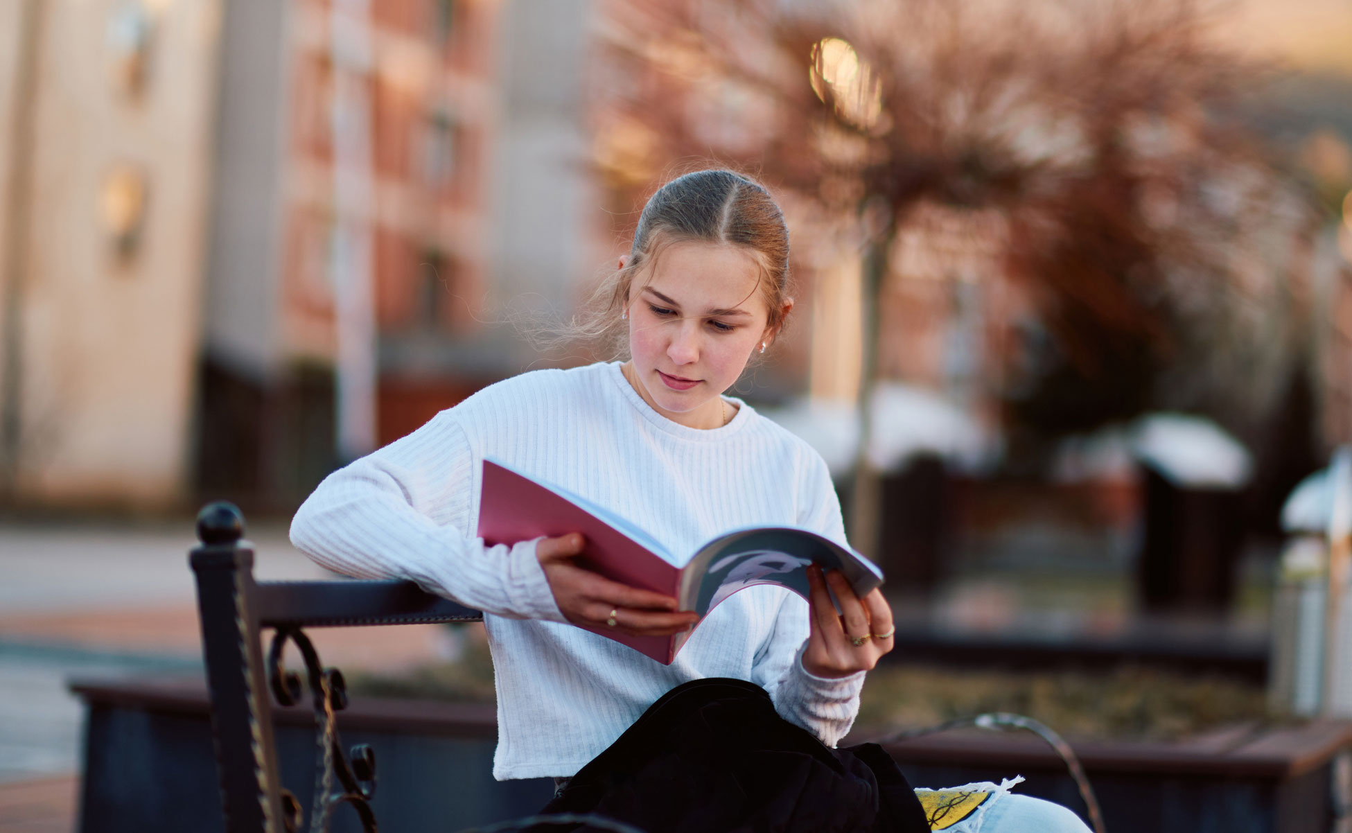Jente leser bok på en benk