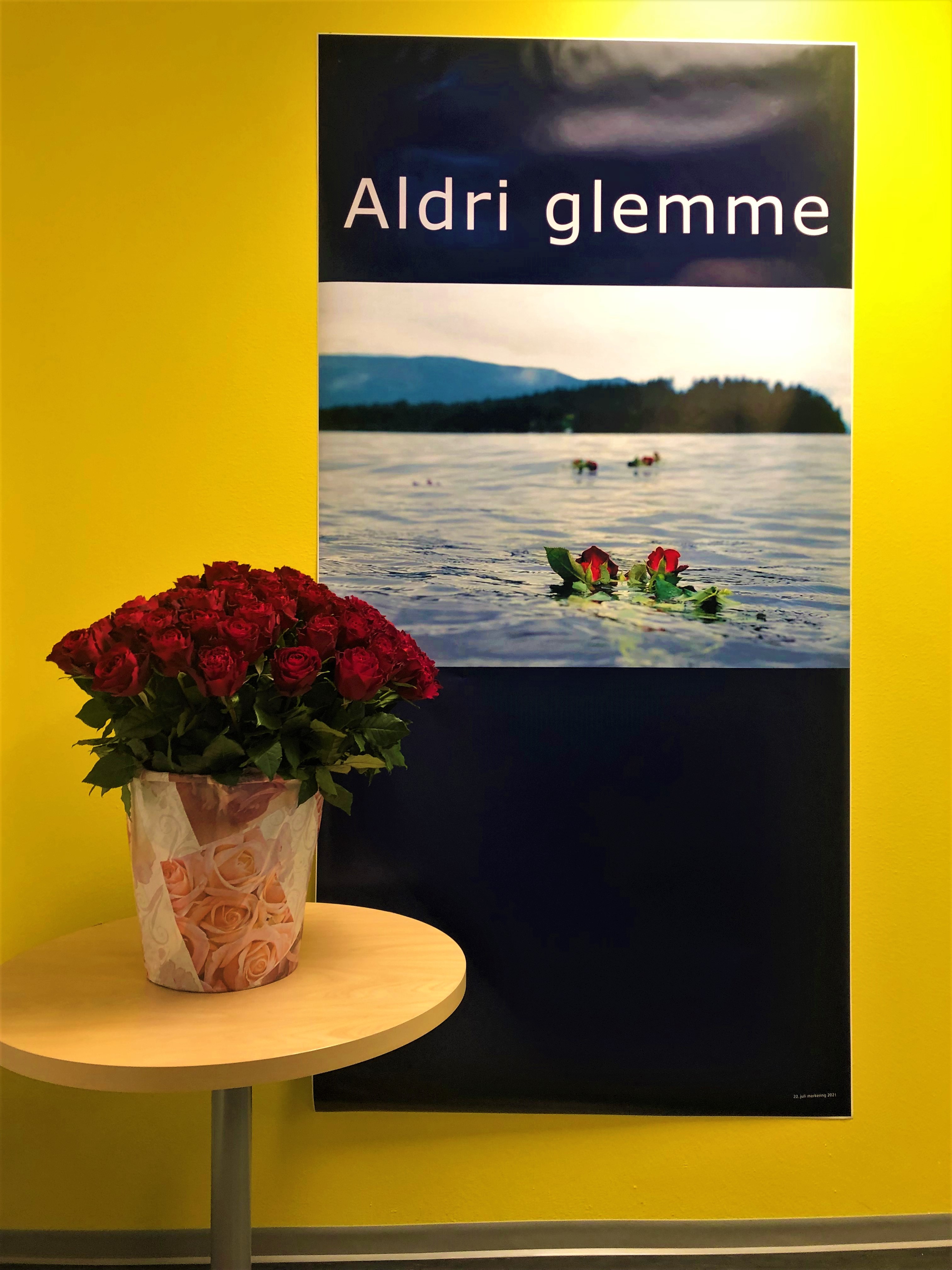 Bilde av 70 roser og en plakat med teksten Aldri Glemme. Bildet på plakaten er av utøya, med røde roser som flyter på vannet.