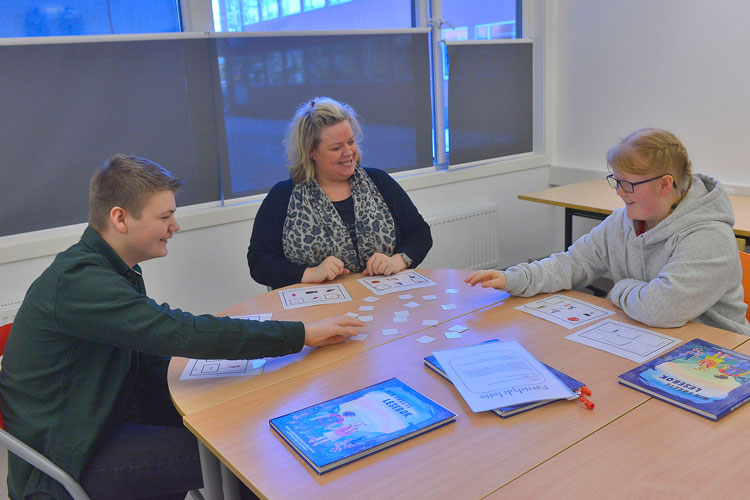 Tre personer sitter rundt et bord og spiller spill.