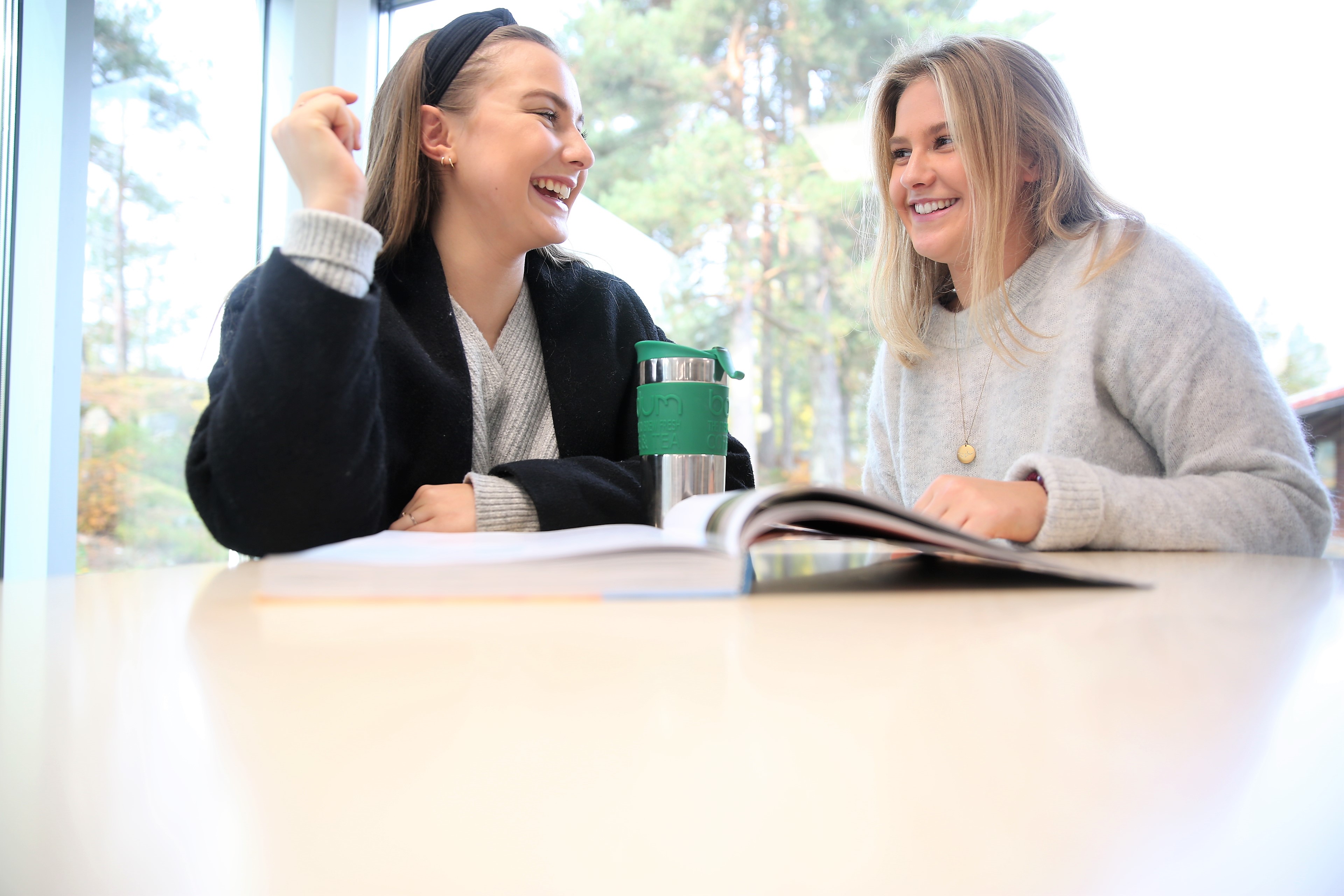 To jenter som sitter sammen og ler.
