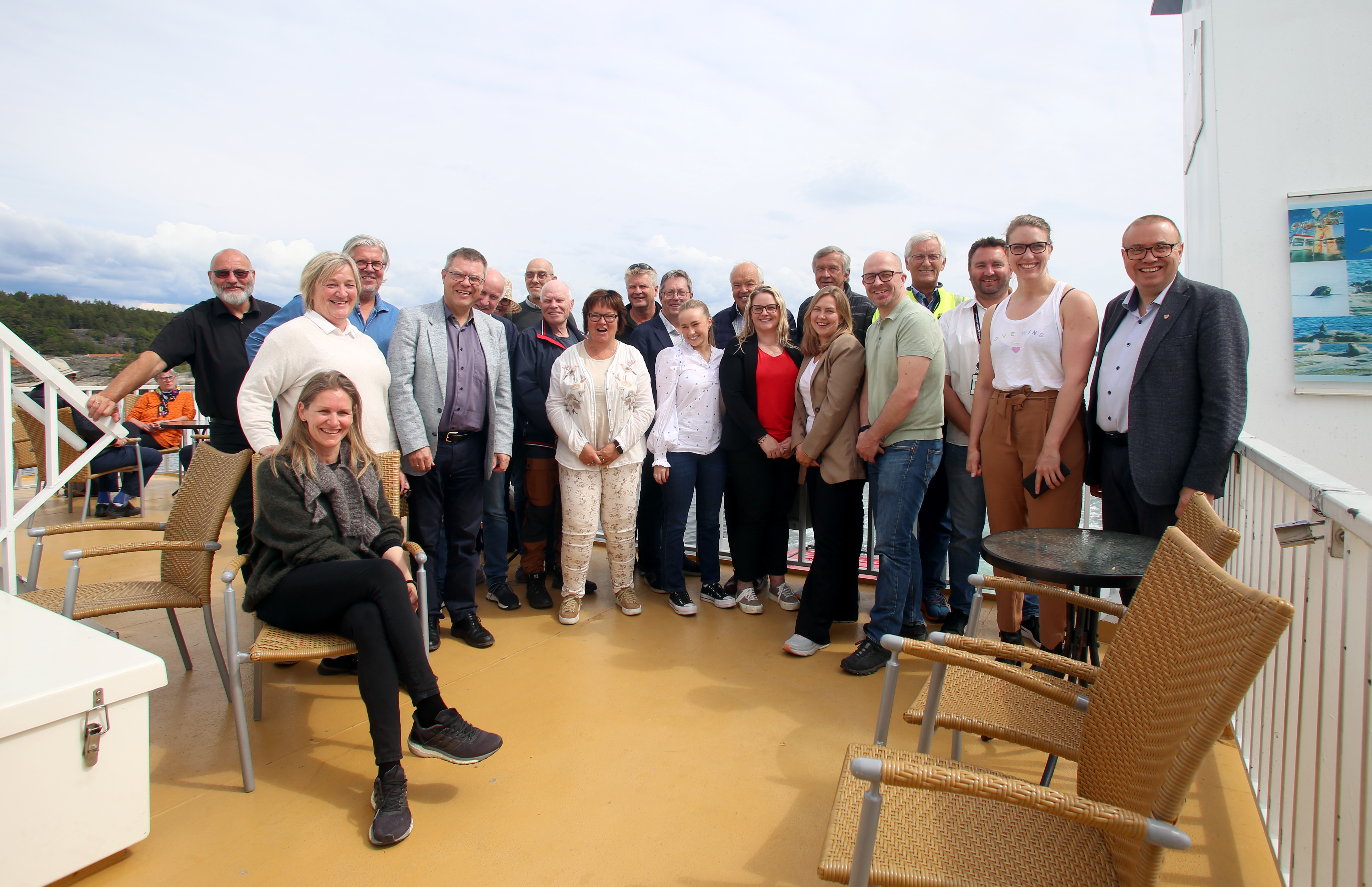 Gruppe mennesker står på ferjedekk, der man kan skimte Jomfruland i bildets bakkant.