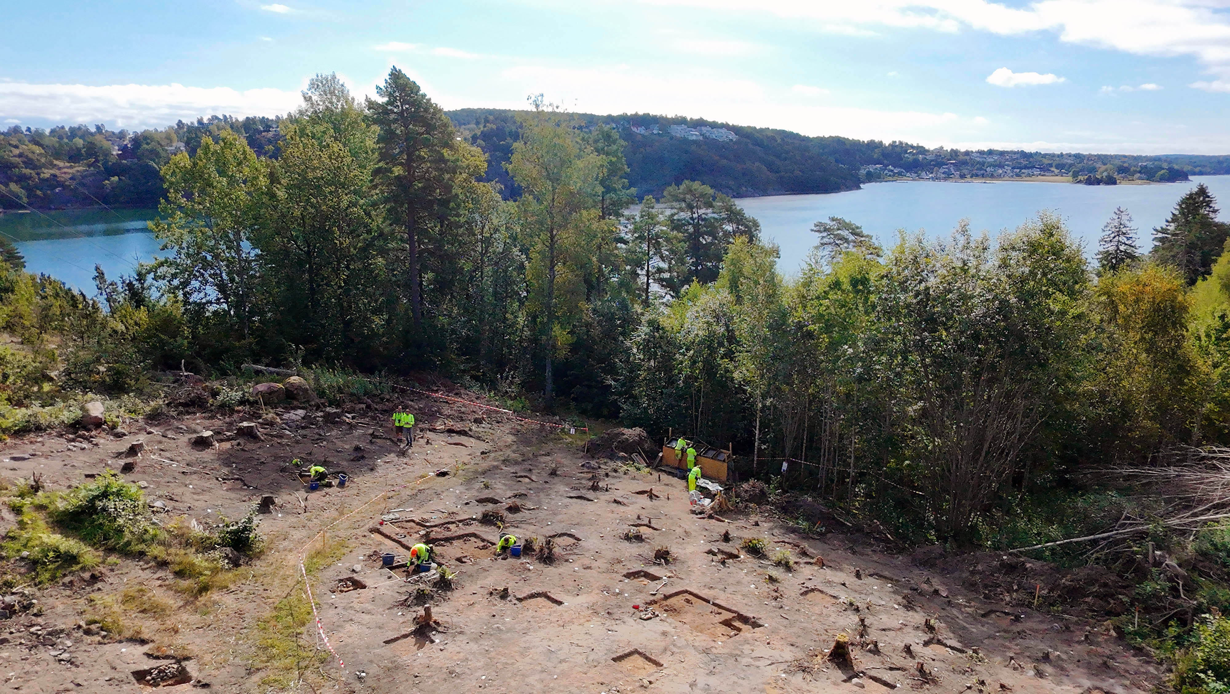 Dronebilde av arkeologer som graver ut steinalderboplass på Smørberg med Vestfjorden i bakgrunnen