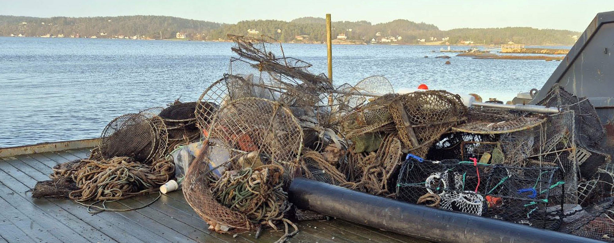 Bildet viser en brygge med en kontainer, og en haug med teiner, tau og ulike fiskeredskaper.