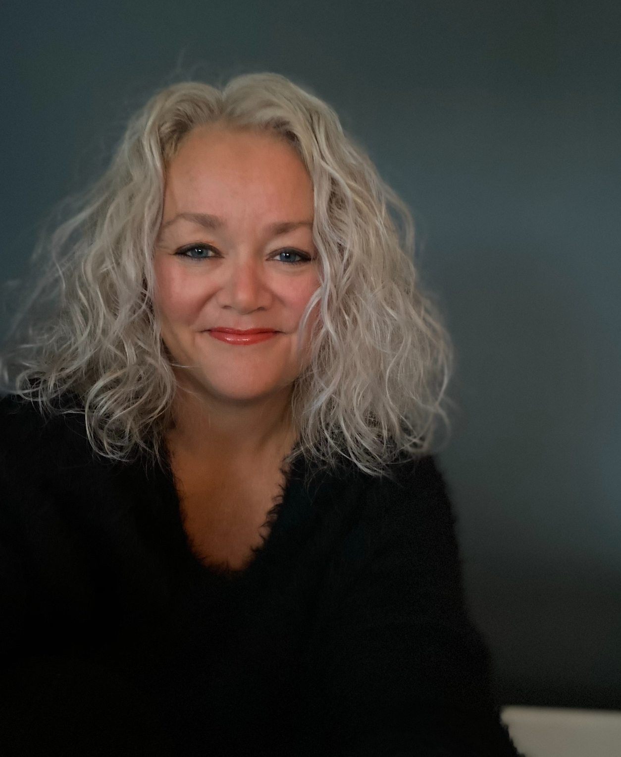 En dame som smiler, har lyst hår med krøller.