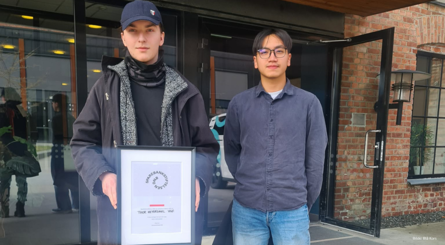 Justin og Tomasz med gavebeviset utenfor en bygning.