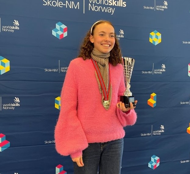 Smildende, glad jente i rosa genser og medalje rundt halsen. Holder en pokal.