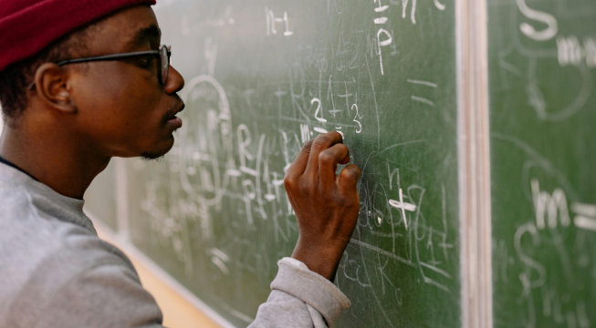 Bilde av mann som skriver regnestykke på grønn tavle.