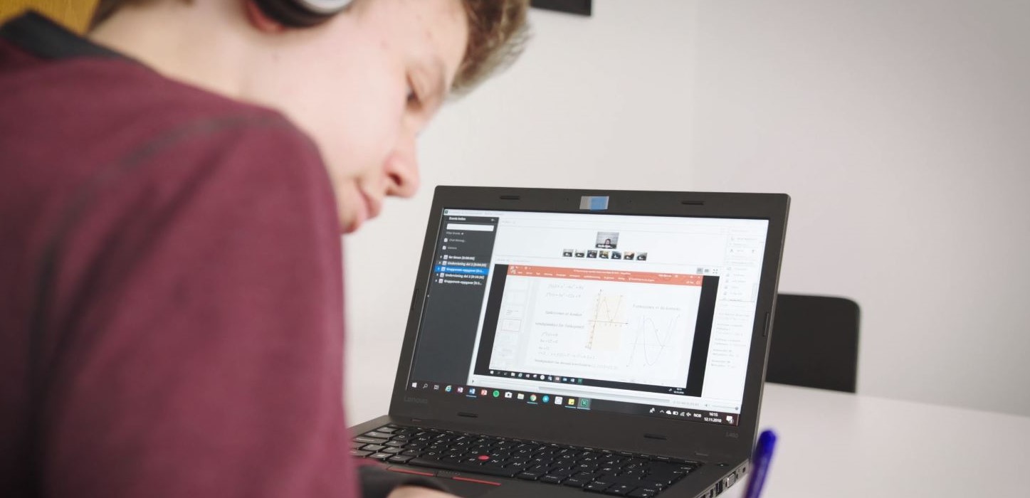 Gutt som ser ned på notater med skjermen på en bærbar PC i bakgrunnen