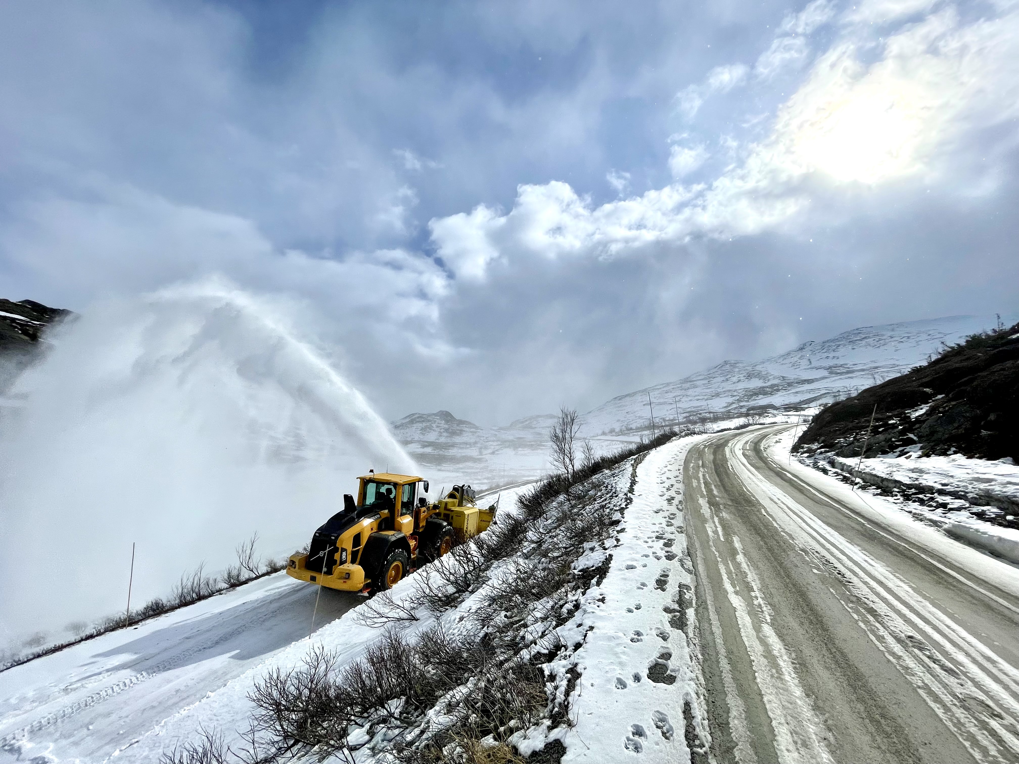 Traktor med snøfreser kjører på vei innover i bildet. Fjellvidde skimtes i bakgrunnen.
