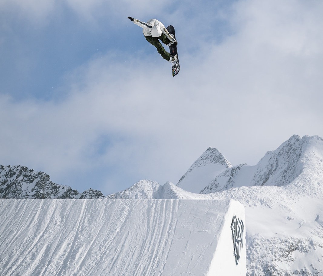 Snowboarder som hopper høyt opp fra et hopp i Alpene.