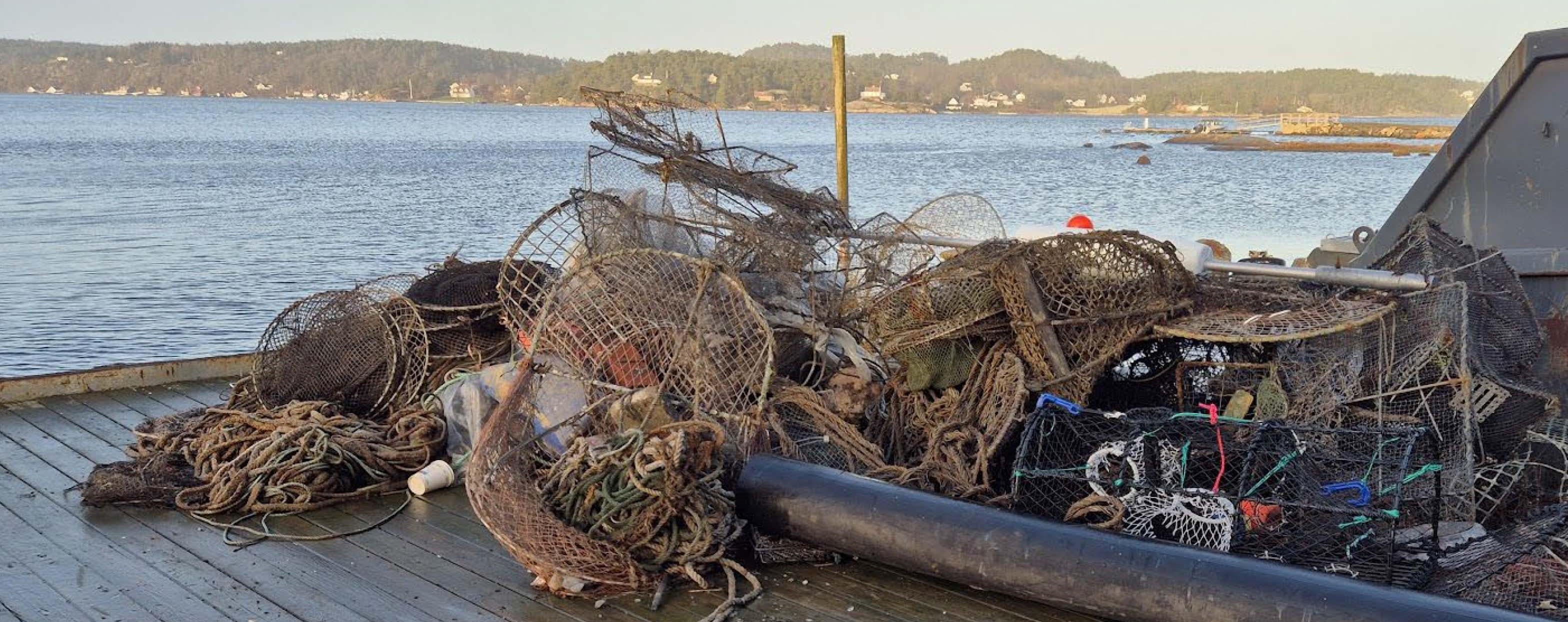 Bildet viser en brygge med en kontainer, og en haug med teiner, tau og ulike fiskeredskaper.